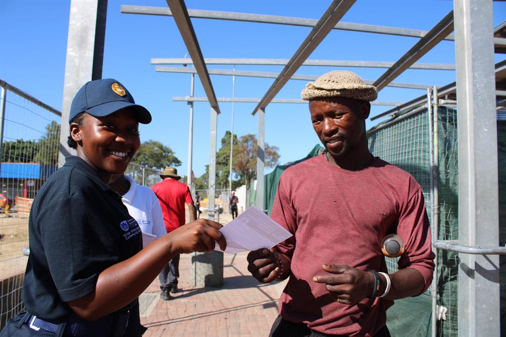 Thimna Zenzile of George Law Enforcement hands Athenkosi Lamani Rhodes a pamphlet on water management measures.